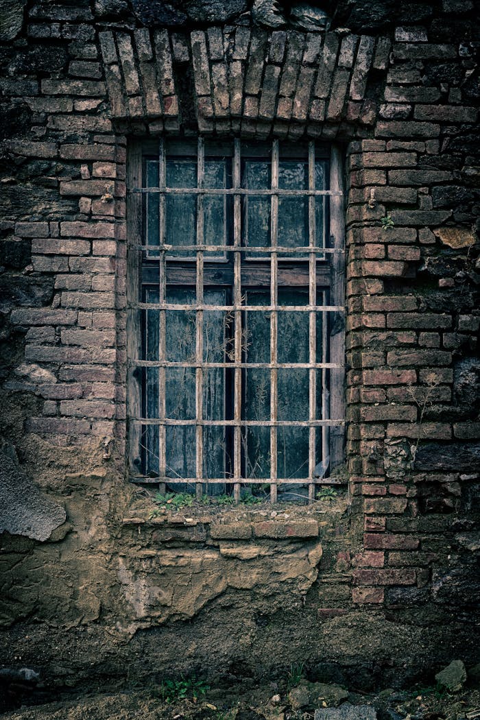 services-01 A moody close-up of an old brick wall featuring a barred window, capturing a sense of nostalgia.