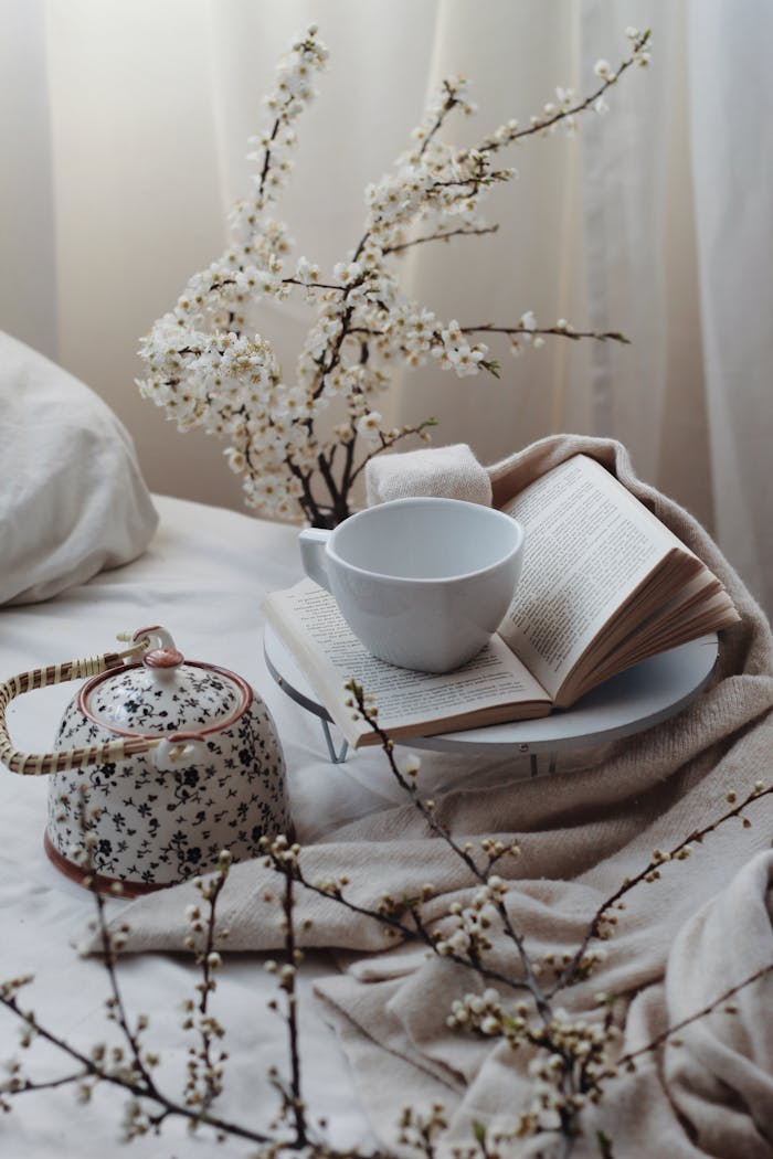 services-03 A warm, inviting scene of tea, book, and blossoms in a softly lit bedroom.